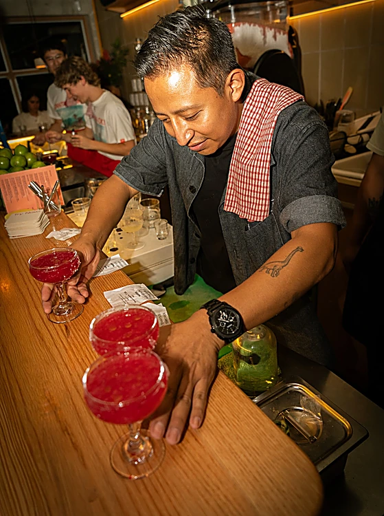 Bartender con toalla de cuadros rojos al hombro sirve margaritas rosas en la barra de roble