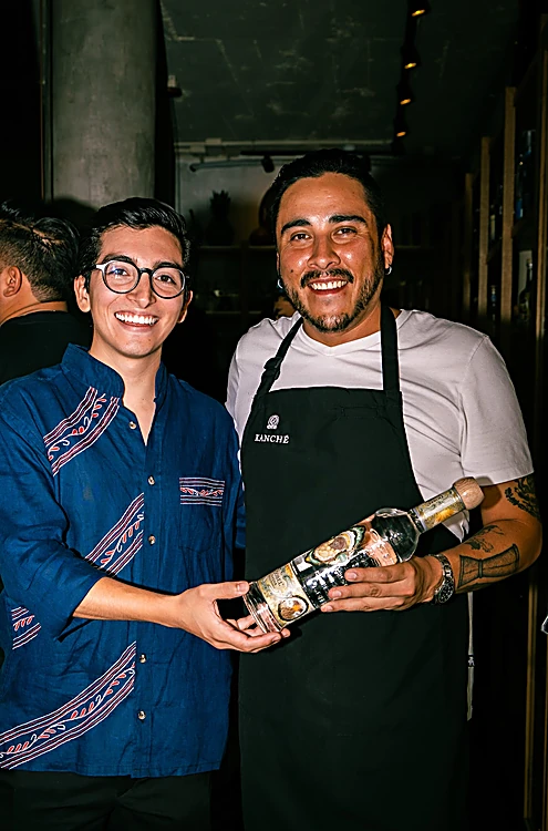 Dos anfitriones de la noche de Izamal sonríen en la barra con una botella de tequila