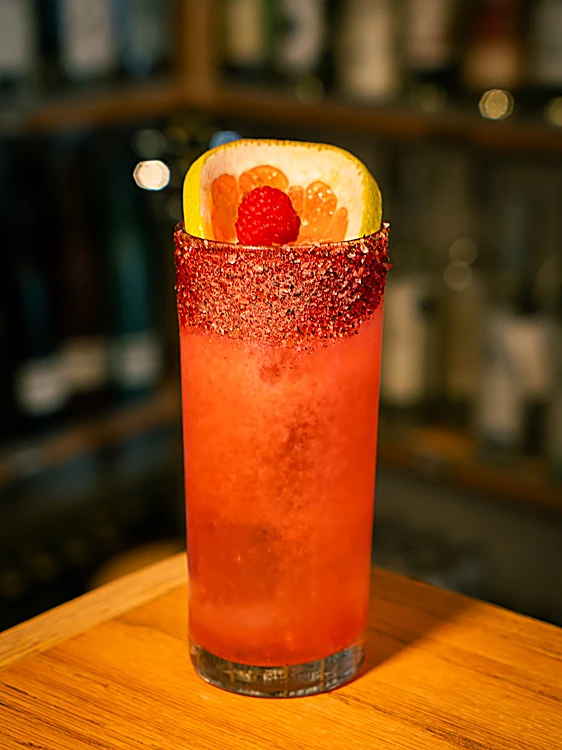 Spiced Berry Paloma: vaso alto rojo con escarcha roja, toronja y frambuesa