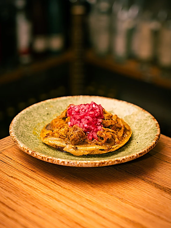 Tostada con carne deshebrada y cebolla morada encurtida en plato de cerámica verde